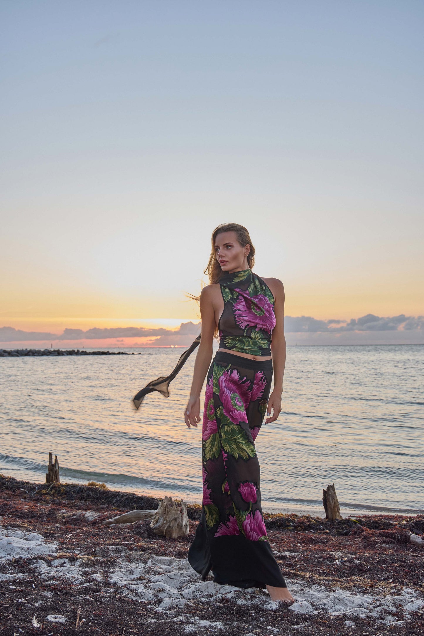 Woman in a floral outfit standing on a beach at sunrise
