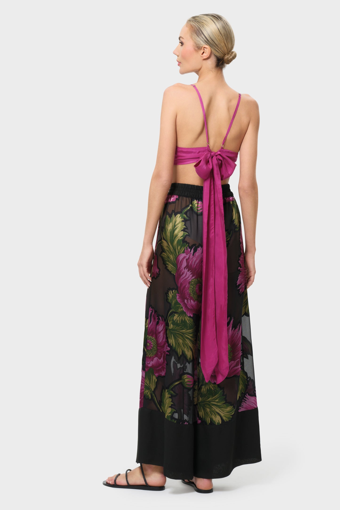 Woman wearing a pink top and black floral pant on a white background