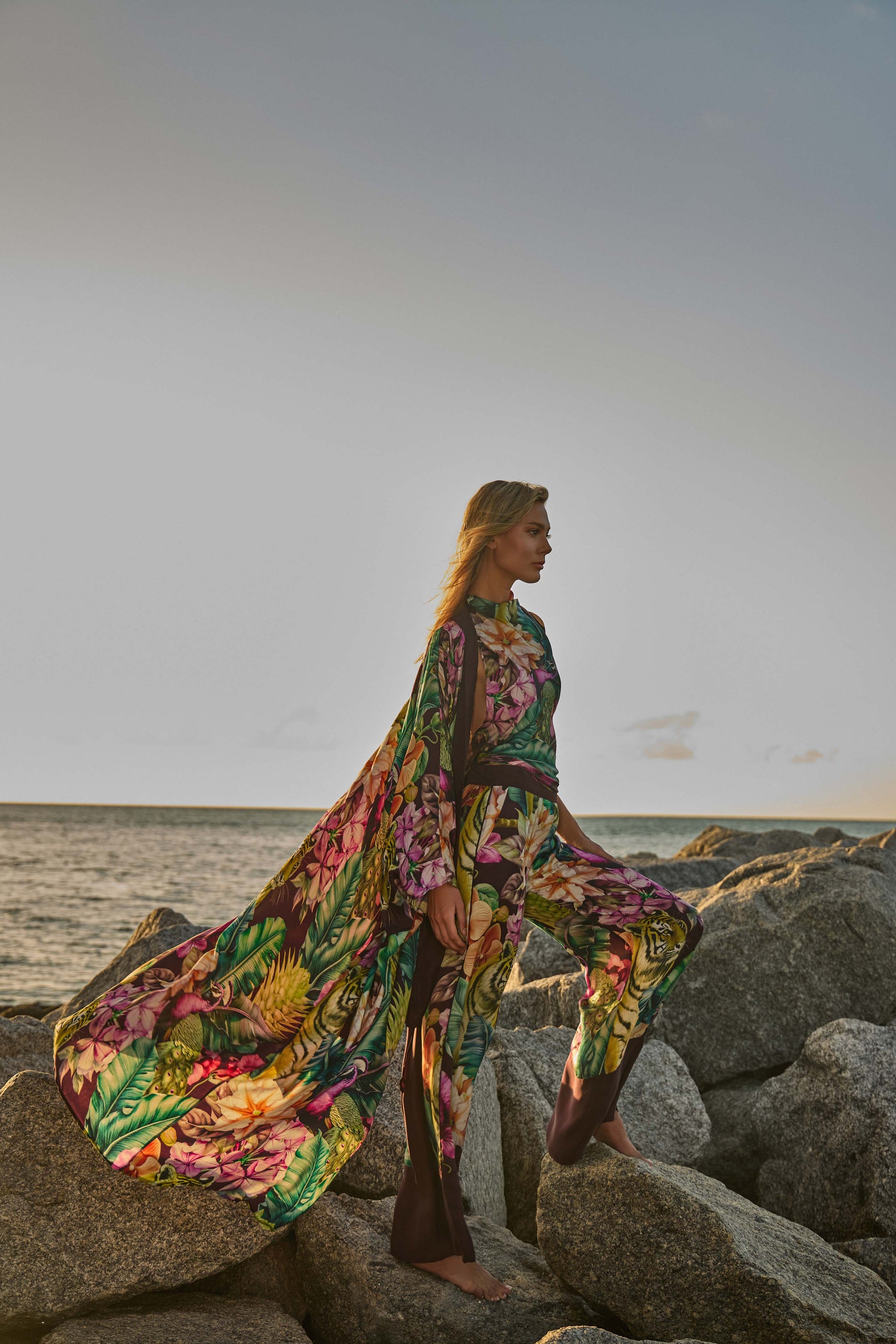 Woman in a colorful floral outfit standing on rocks by the sea