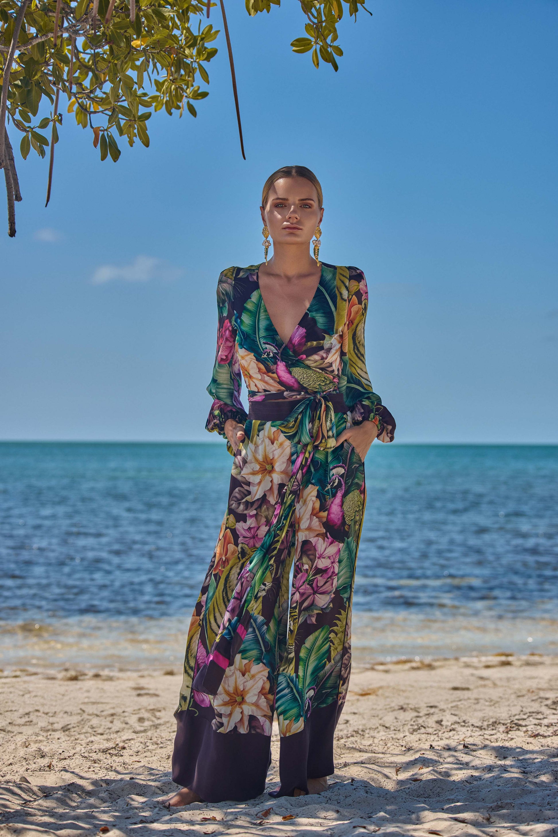 Woman in a colorful floral outfit standing on a beach with ocean and sky in the background