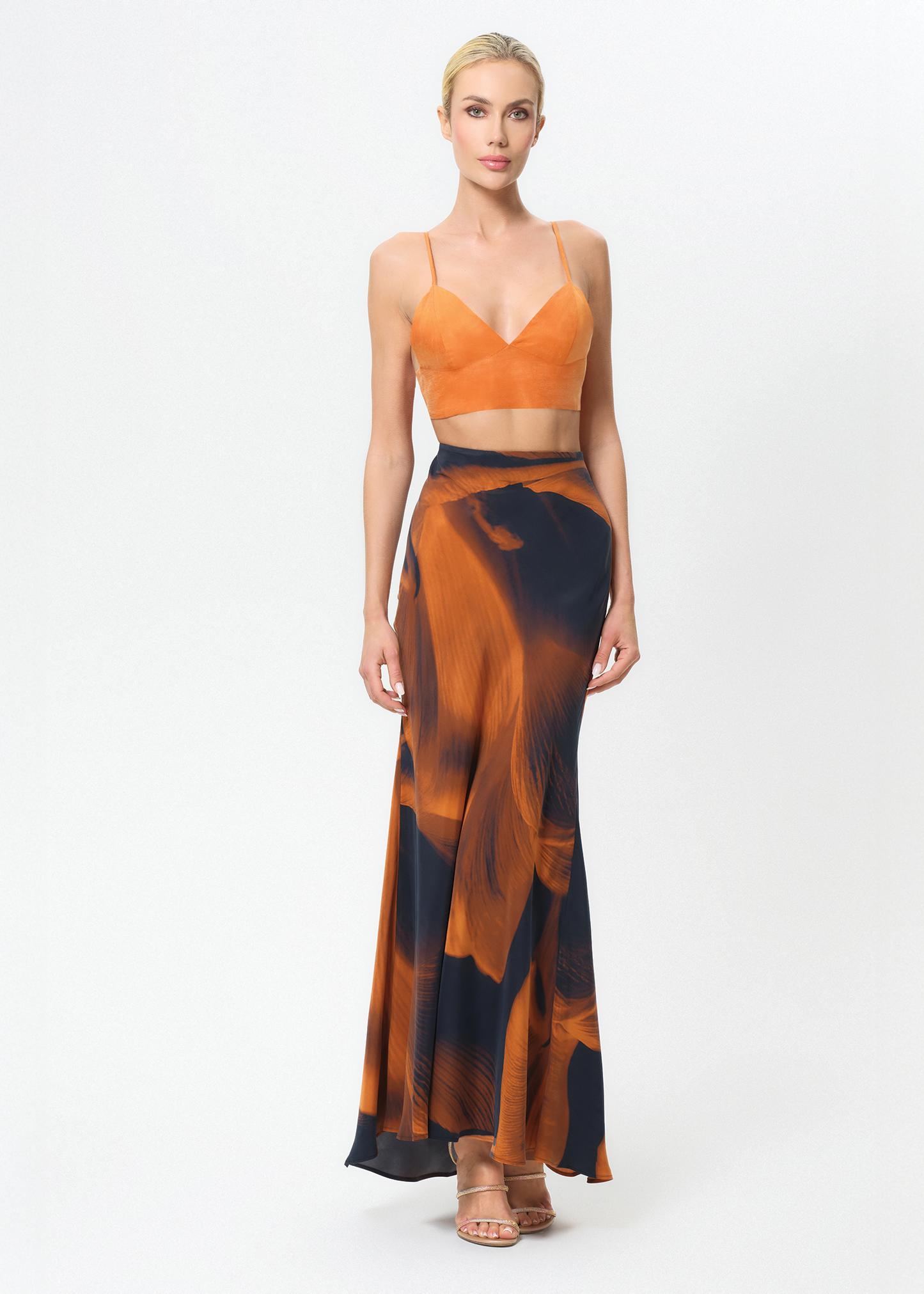 Woman wearing an orange top and black and orange patterned skirt on a white background