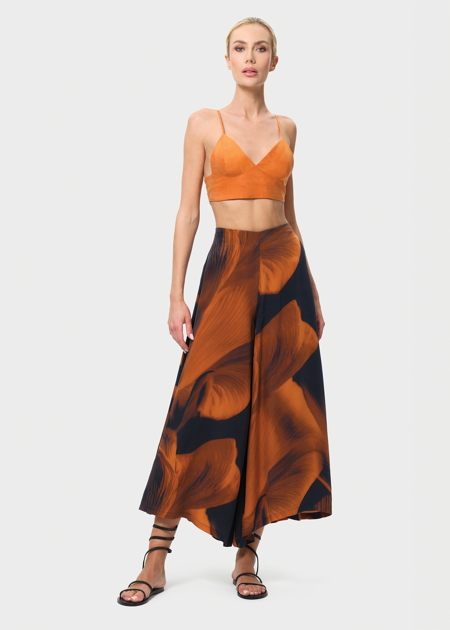 Woman wearing an orange top and patterned skirt on a white background