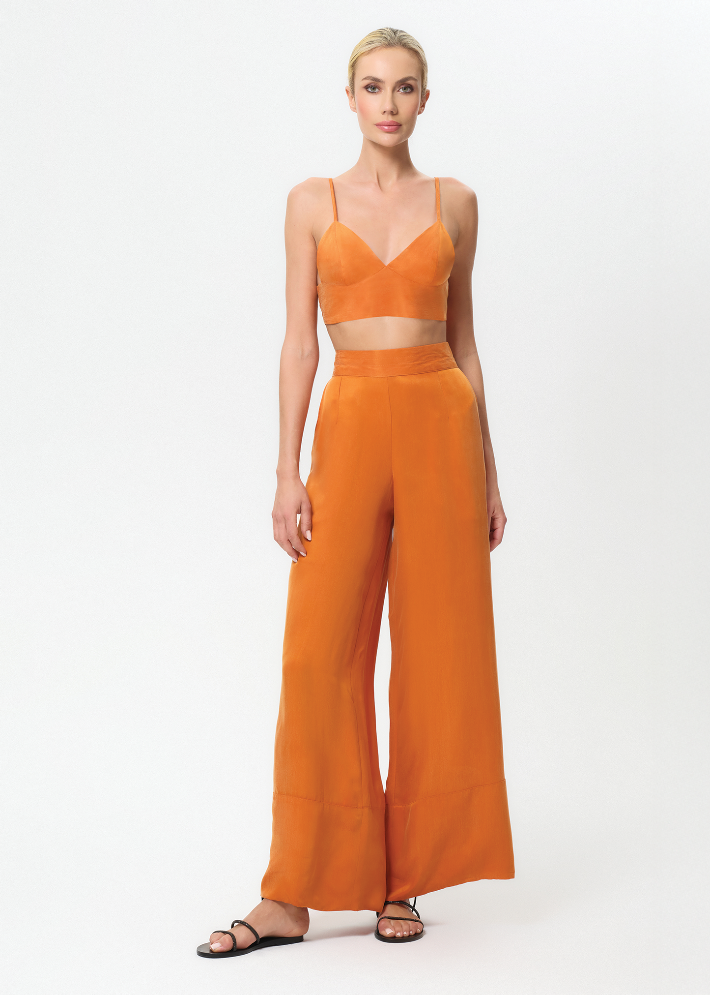 Woman wearing an orange outfit with a top and wide-leg pants on a white background