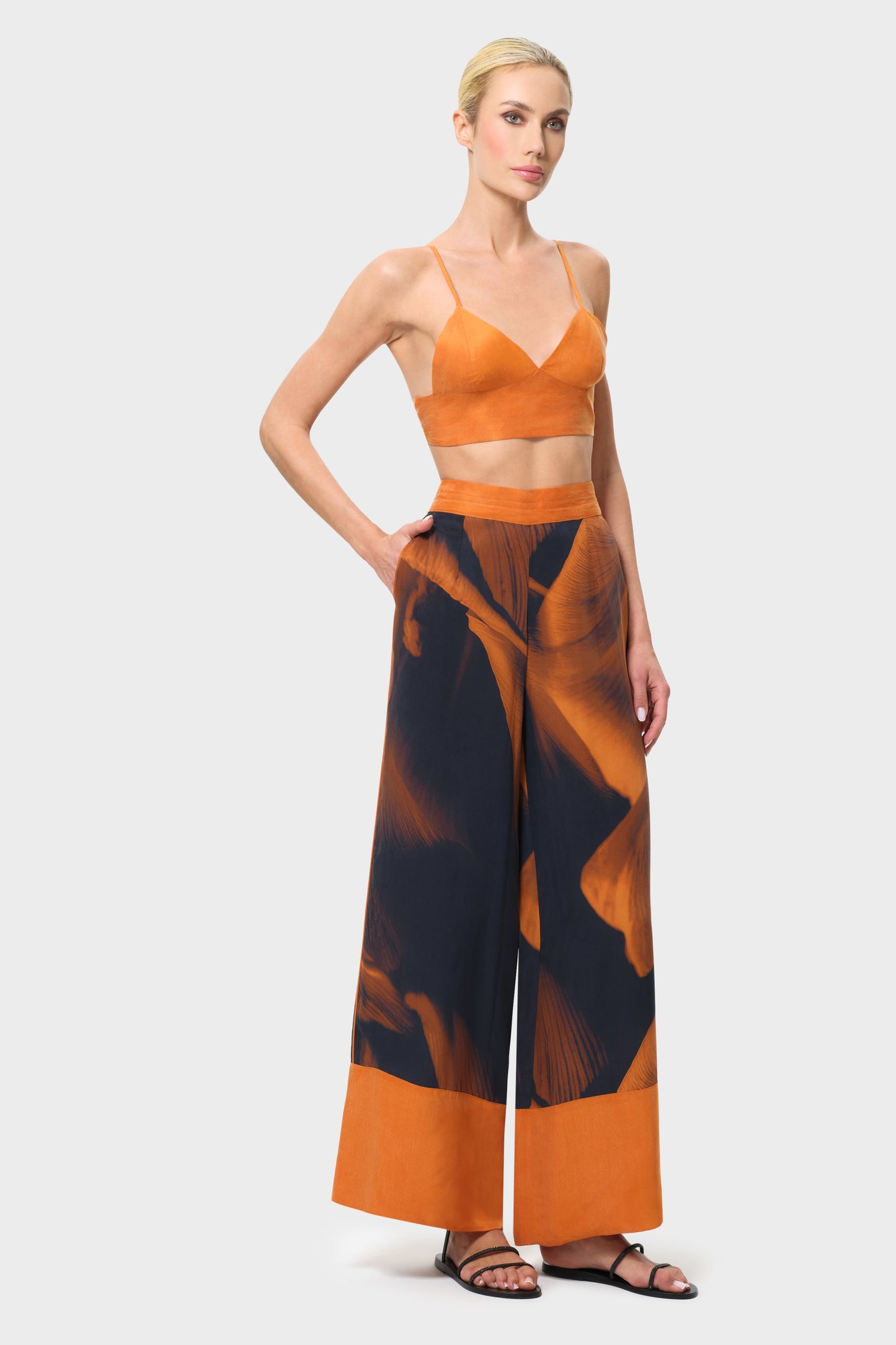 Woman wearing an orange top and patterned pants on a white background