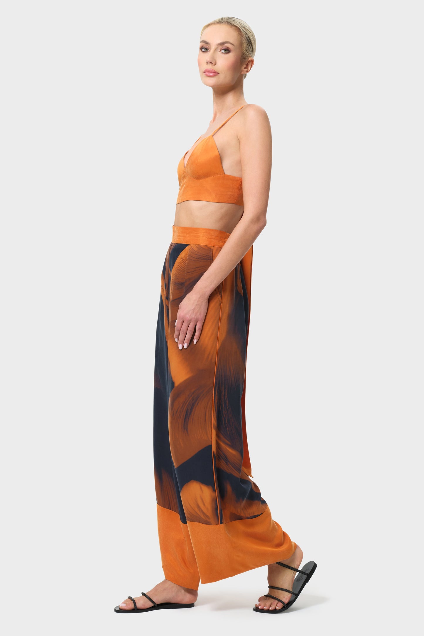 Woman wearing an orange top and patterned pants on a white background