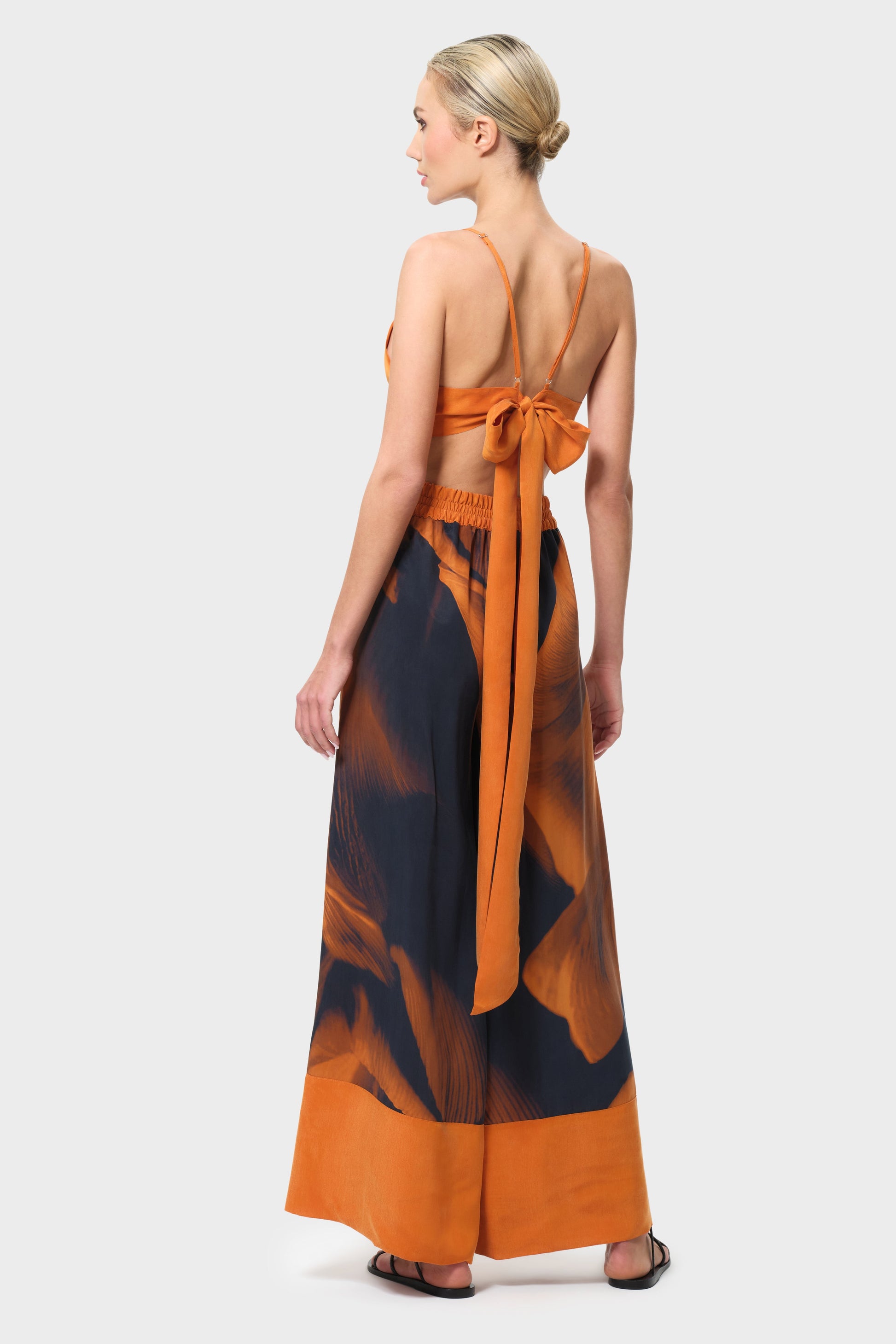 Woman wearing an orange top and patterned pants on a white background