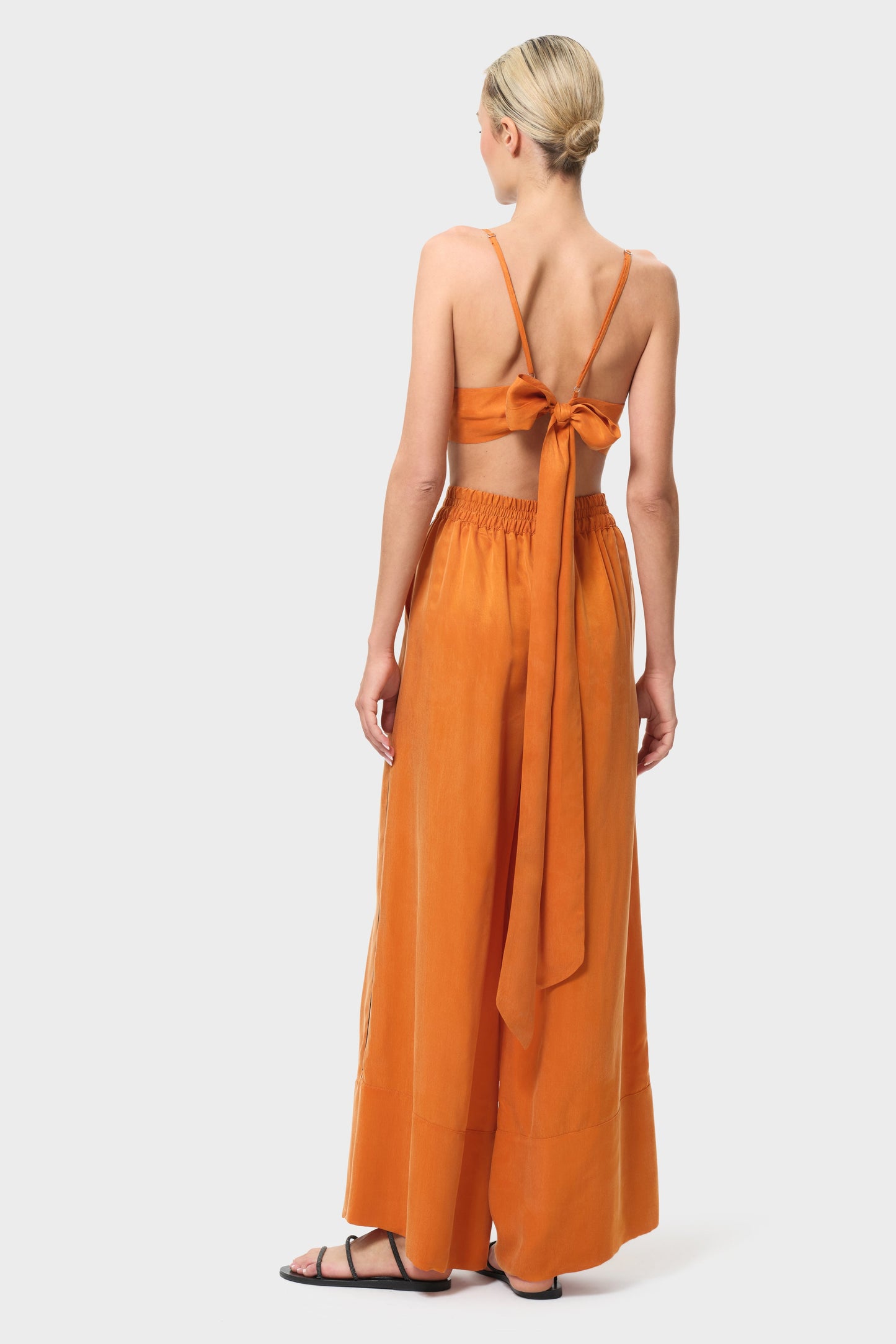 Woman wearing an orange outfit with a top and wide-leg pants on a white background