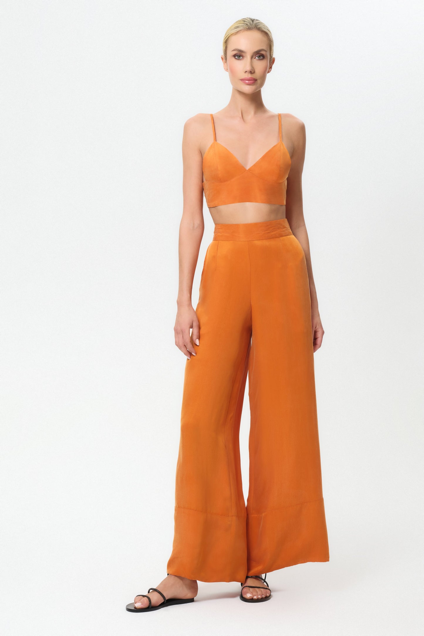 Woman wearing an orange outfit with a top and wide-leg pants on a white background