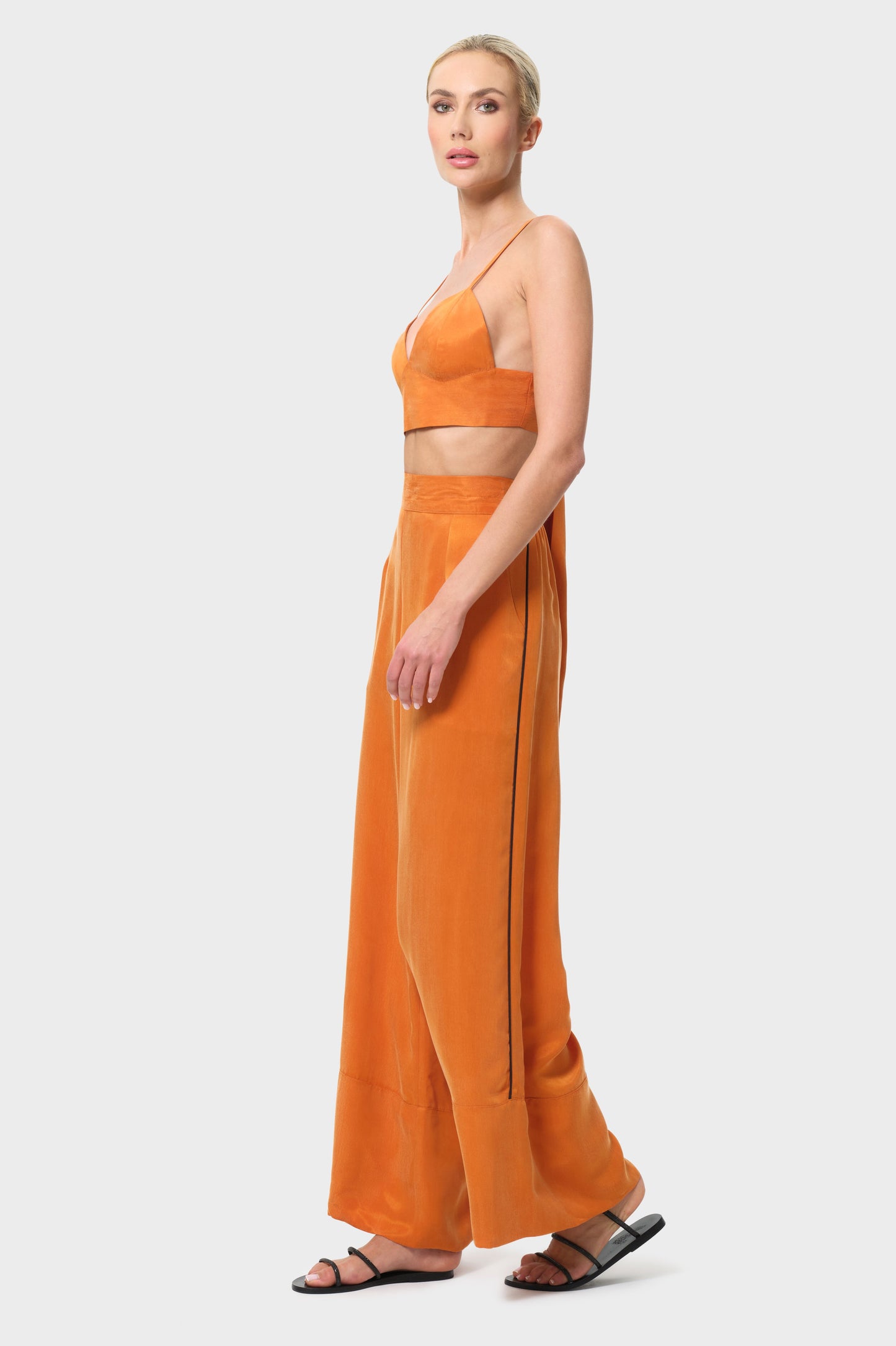 Woman wearing an orange outfit with a top and wide-leg pants on a white background