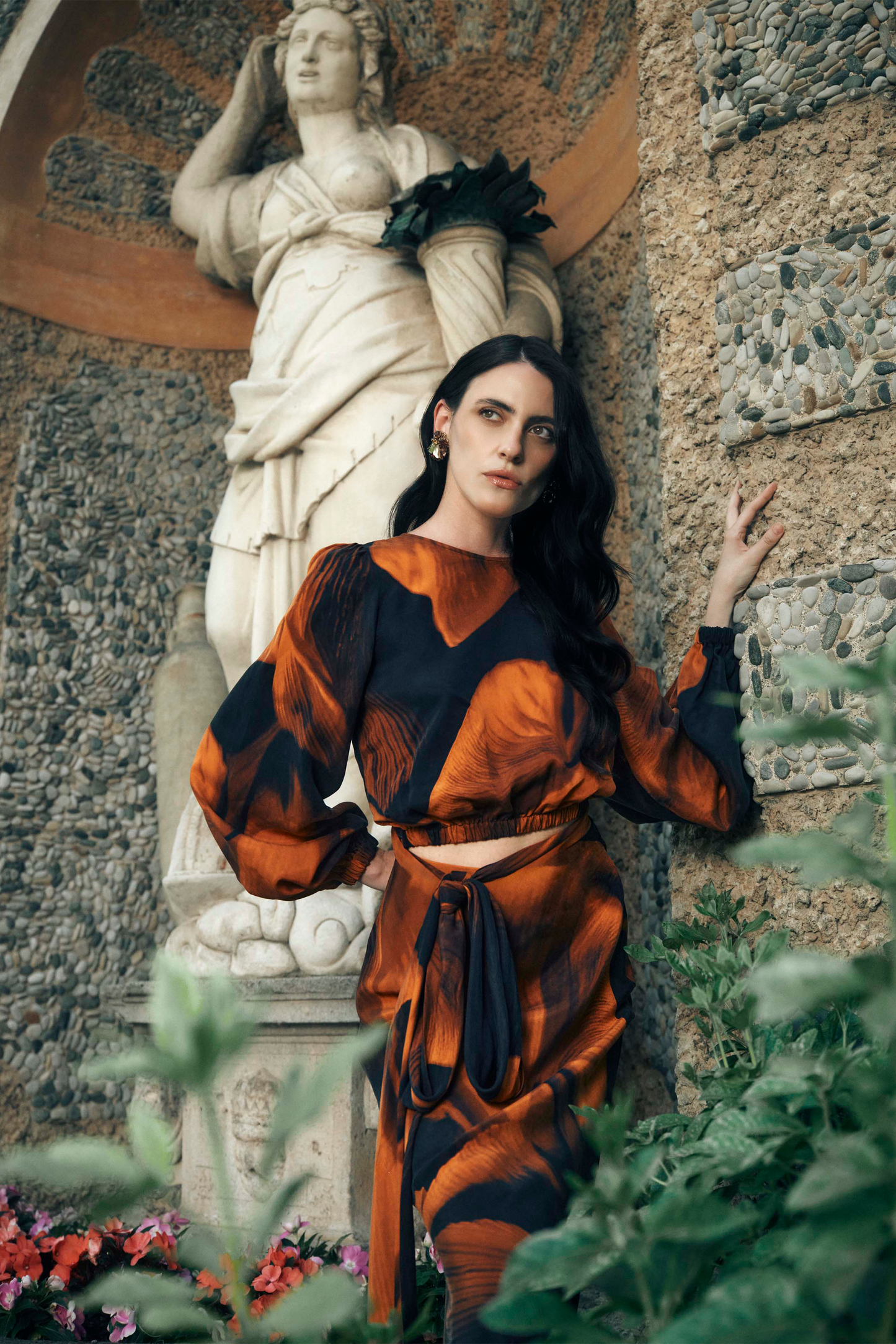 Woman in an orange and black patterned outfit standing in front of a classical statue.
